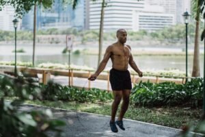 A man enjoys an energetic workout by jumping rope in a lush city park on a sunny day.