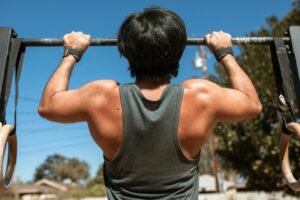 Man doing pull-ups on a bar outdoors, emphasizing fitness and strength.