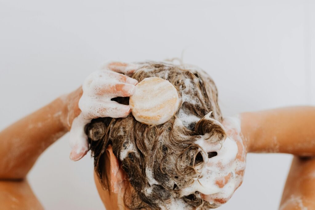 Close-up of a person washing their hair with soap bar and foam, focusing on hands and hair.