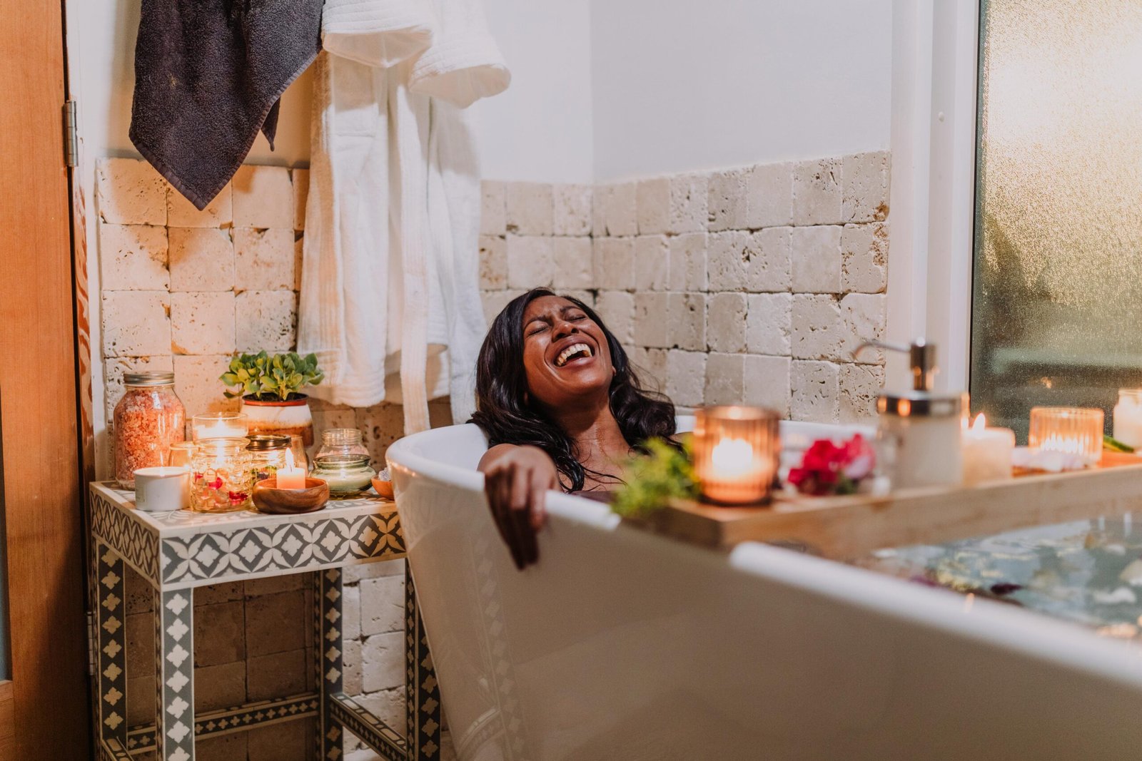 A joyful woman soaking in a serene bath surrounded by candles and warm ambiance.
