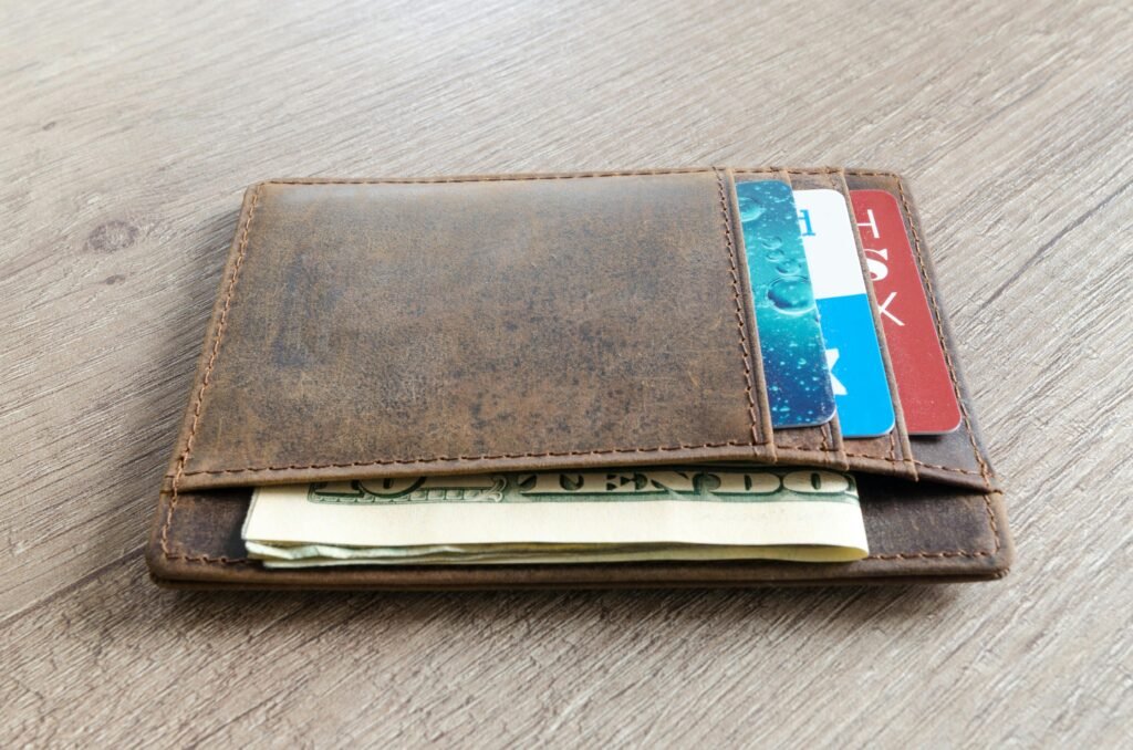 A brown leather wallet with cash and credit cards on a wooden surface.