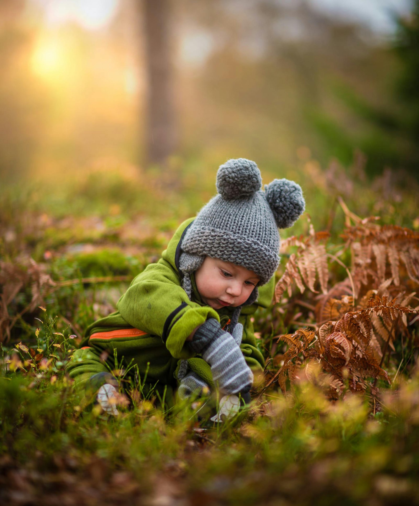 A cute baby in a knit hat and green outfit exploring nature during sunset.