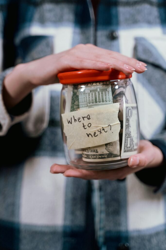 A person holds a savings jar filled with money and a note that says 'Where to next?' symbolizing travel savings.
